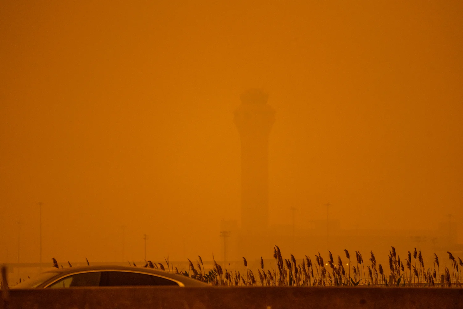Une voiture et la silhouette d’une tour presque effacées par une épaisse fumée orange.
