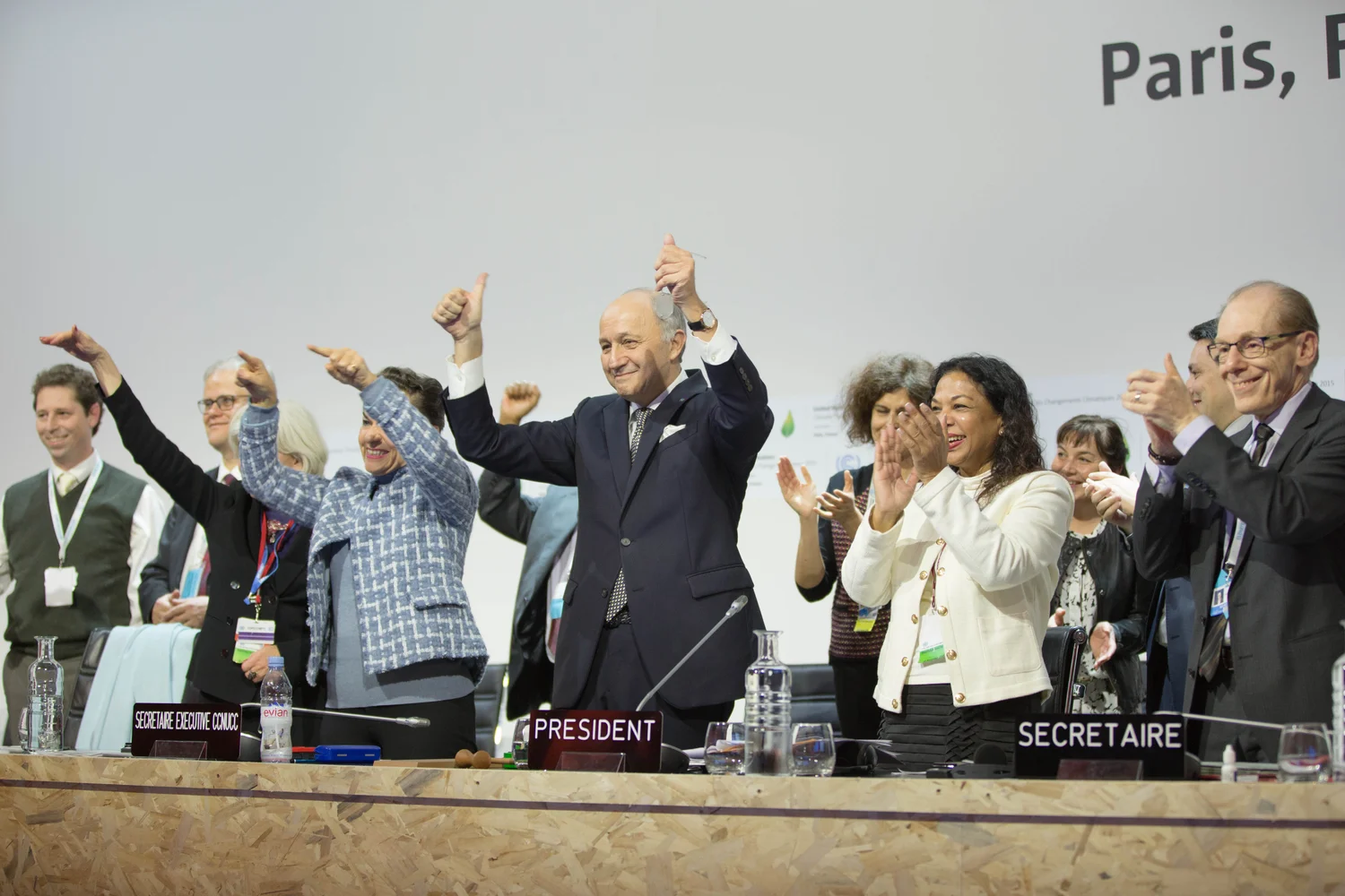 Laurent Fabius lève les pouces, entouré de responsables qui applaudissent à la COP21.